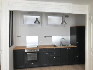 a kitchen with black cabinets and a sink and two lights at La Savane du Donjon in Rouen