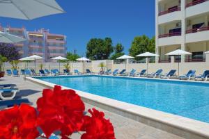 una piscina en un hotel con flores rojas en primer plano en Hotel Alba en Monte Gordo