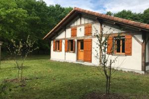 una pequeña casa blanca con puertas marrones y un árbol en Spa et détente au cœur de la forêt des Landes, en Luglon