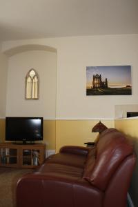 sala de estar con sofá de cuero y TV de pantalla plana en No2 Abbey View Apartment, en Whitby