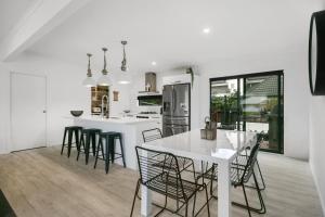 a white kitchen with a white table and chairs at Sky Above Beach Below - Waihi Beach Holiday Home in Waihi Beach