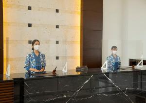 two men wearing face masks standing behind a counter at Ala Mahaina Condo Hotel in Motobu