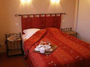 a red bed with a tray of dishes on it at Logis L'Auberge du Quercy Blanc in Molières