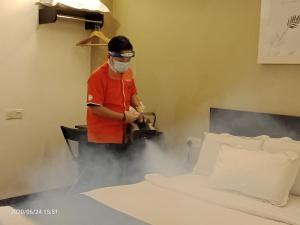 um homem com uma máscara num quarto a fazer uma cama em Orange Hotel Kota Kemuning @ Shah Alam em Shah Alam