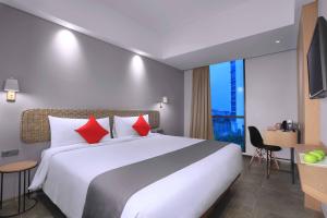 una habitación de hotel con una gran cama blanca con almohadas rojas en Neo Hotel Puri Indah, en Yakarta