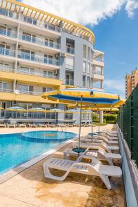 a pool with lounge chairs and umbrellas next to a building at Apartments Kristal Beach Nessebar in Nesebar