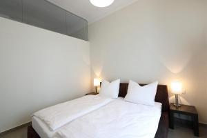 a bedroom with a bed with white sheets and two lamps at Stylische Cityapartments Benedikt in Klagenfurt