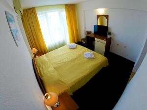 um pequeno quarto com uma cama amarela e um espelho em Hotel Lotos em Kiten