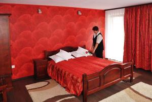 um homem ao lado de uma cama vermelha num quarto em Pensiunea Filonul de Aur em Aktenburg