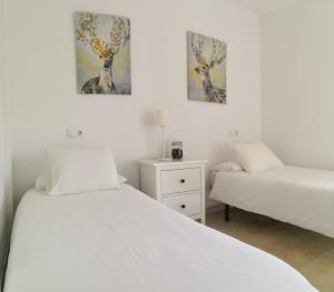 two beds in a white room with paintings on the wall at Muro de los Navarros 26-Apartamentos in Seville