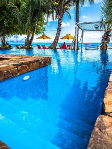 - une piscine sur la plage avec des personnes assises sous des parasols dans l'établissement Hotel ECOLODGE LE RAVORAHA, sur l'île Sainte-Marie