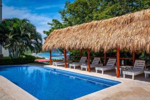a resort swimming pool with chairs and a straw umbrella at Fifth-Floor Condo with Breathtaking Ocean Views, Stylish Interior & Prime Location Near Flamingo Beach in Playa Flamingo
