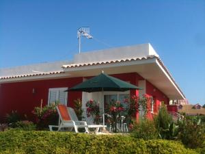 a red house with two chairs and an umbrella at 2 bedrooms villa with sea view enclosed garden and wifi at Sciacca 5 km away from the beach in Sciacca