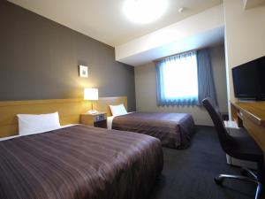 Habitación de hotel con 2 camas, escritorio y TV. en Hotel Route-Inn Obihiro Ekimae, en Obihiro