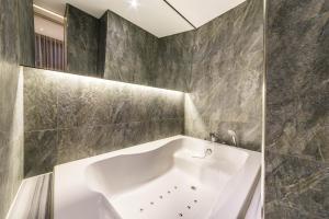 a white bath tub in a bathroom with gray tiles at Guwol Hotel in Incheon
