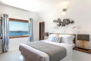 a white bedroom with a bed and a window at 180° Caldera by Stylish Stays in Firostefani