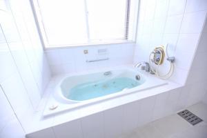 a white tiled bathroom with a tub with a window at Hotel Marital Sousei Kurume in Kurume