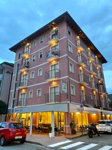 un gran edificio rosa con coches estacionados frente a él en Hotel Rosa Caorle, en Caorle