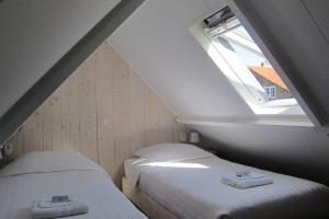 two beds in a attic room with a window at Omas kleine huisje in Veere