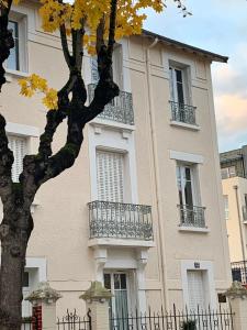 ein Gebäude mit Balkonen und einem Baum davor in der Unterkunft La Villégiature et la Maisonnette in Vichy