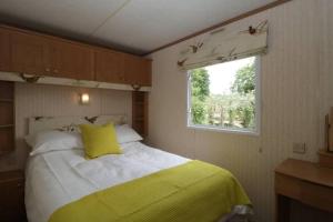 ein Schlafzimmer mit einem Bett mit gelbem Kissen und einem Fenster in der Unterkunft The Nest - Family friendly caravan nr Glastonbury & Street in Somerton