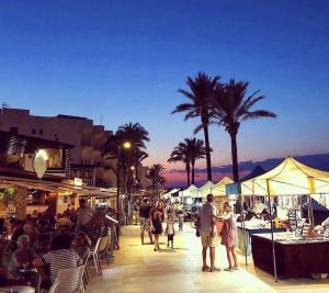 eine Gruppe von Menschen, die auf einem Markt mit Palmen spazieren in der Unterkunft Bella Paula in Es Pujols