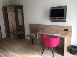 Cette chambre dispose d'un bureau, d'une télévision et d'une chaise rose. dans l'établissement Hotel am Kunnerstein, à Augustusburg