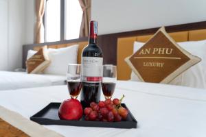 ハロンにあるAn Phú Hạ Long Luxury Hotelのベッドの上にワイン2杯とフルーツを用意したトレイ