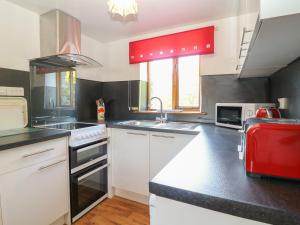 eine Küche mit weißen Schränken und einer roten Decke in der Unterkunft Swallow Cottage in Bude