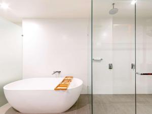 uma casa de banho branca com uma banheira e uma cabina de duche em vidro. em Novotel Brisbane South Bank em Brisbane