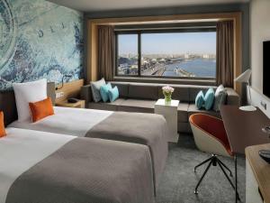 a hotel room with two beds and two windows at Mövenpick Hotel Amsterdam City Centre in Amsterdam