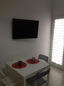 une table blanche avec deux chaises et une télévision murale dans l'établissement Marconi’ home, à Margherita di Savoia