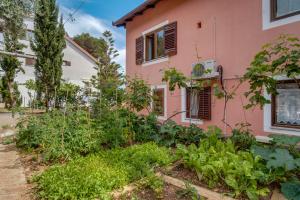 a garden in front of a pink house at Apartments Villa Julija in Mali Lošinj