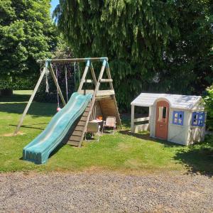 un parco giochi con scivolo e una casetta per i giochi di Le Cottage de L Abbaye a Lonlay-lʼAbbaye