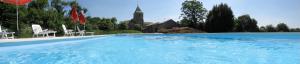 una gran piscina con sillas blancas y una iglesia. en La Ferme de l'Eglise, en Vanzay
