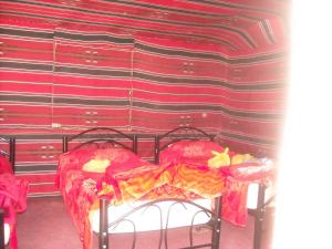 two beds in a room with a red wall at Bedouin House Camp in Wadi Rum