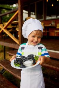młody chłopiec w kapeluszu szefa kuchni trzymający talerz jedzenia w obiekcie Каньон w mieście Grushevtsy