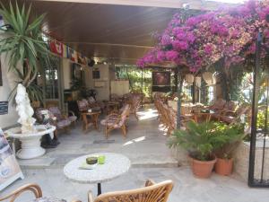 eine Terrasse mit Tischen, Stühlen und lila Blumen in der Unterkunft Harry's Bar & Apartments 1 in Acharavi
