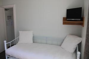 Elle comprend un petit lit avec des draps blancs et une télévision murale. dans l'établissement Logis Hotel De Paris, à Jaligny-sur-Besbre