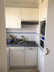 a small kitchen with white cabinets and a sink at Face à la mer à Cabourg in Cabourg