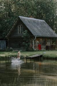 a woman swimming in the water in front of a house at Viesu nams Lauciņi in Lāde