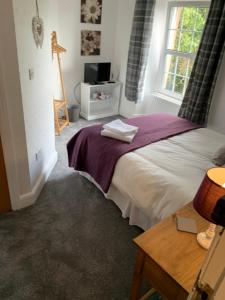 ein Schlafzimmer mit einem Bett mit einer lila Decke und einem Fenster in der Unterkunft DOVENBY SHIP in Tallentire