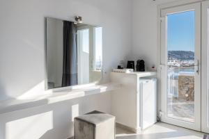 Cette chambre blanche dispose d'une fenêtre et d'un tabouret. dans l'établissement Magic View Suites Mykonos, à Mykonos