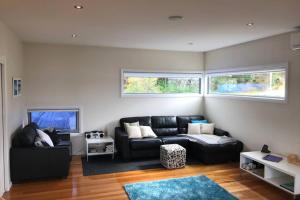 a living room with a black couch and two windows at Amazing Ansons Bay Absolute Waterfront Beach House in Ansons Bay