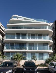 un edificio blanco alto con coches estacionados frente a él en Beach Lux Apartment, en Haifa