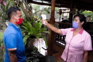 a woman wearing a mask taking a picture of a man with a plant at Murni's Houses & Spa in Ubud