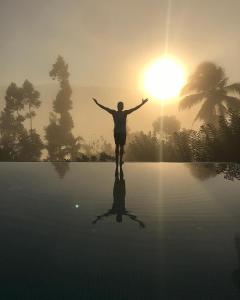 Aarunya Nature Resort and Spa في كاندي: شخص يقف على الماء مع الشمس في الخلفية