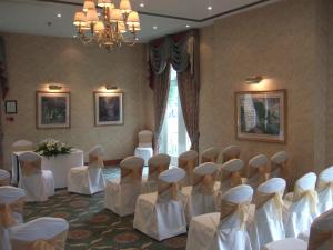 a room with white chairs and tables and a chandelier at Coulsdon Manor Hotel and Golf Club in Croydon