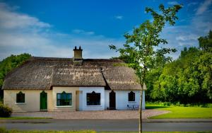 een klein wit huis met een rieten dak bij Cottage 33 Old Killarney Village Killarney in Killarney
