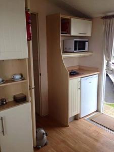 una pequeña cocina con armarios blancos y microondas en Haven Devon Cliffs Caravan en Budleigh Salterton